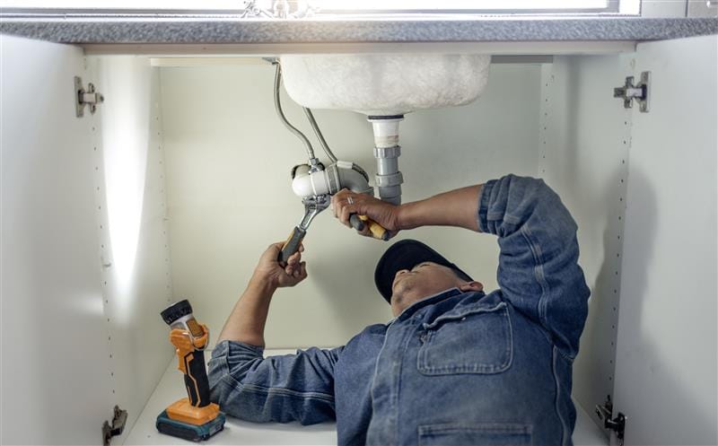 Plumber repairing pipes beneath a bathroom sink in Salinas