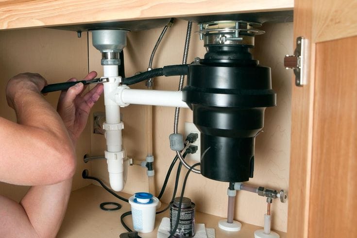 Plumber installing a garbage disposal beneath a kitchen sink in Salinas