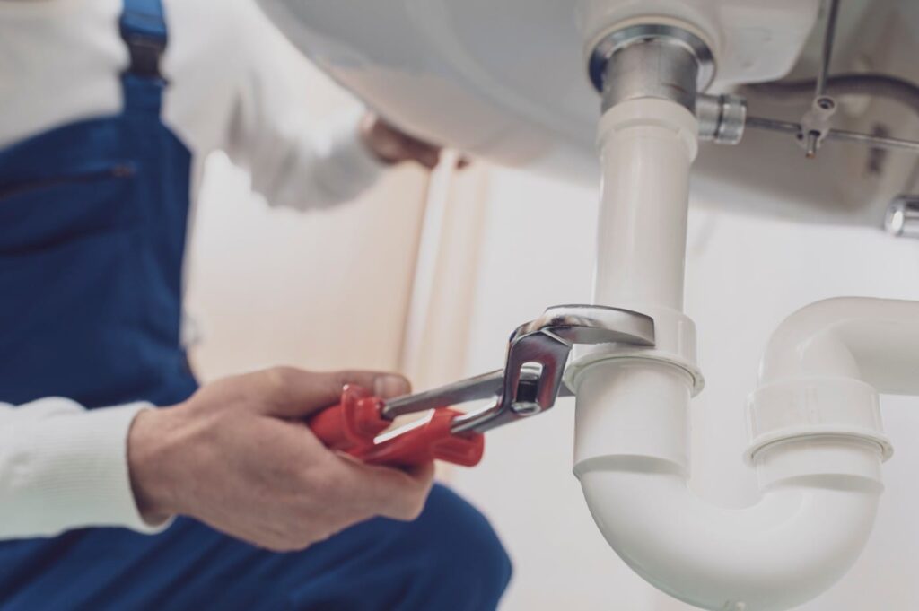 Plumber repairing a white drain pipe beneath a sink in Salinas
