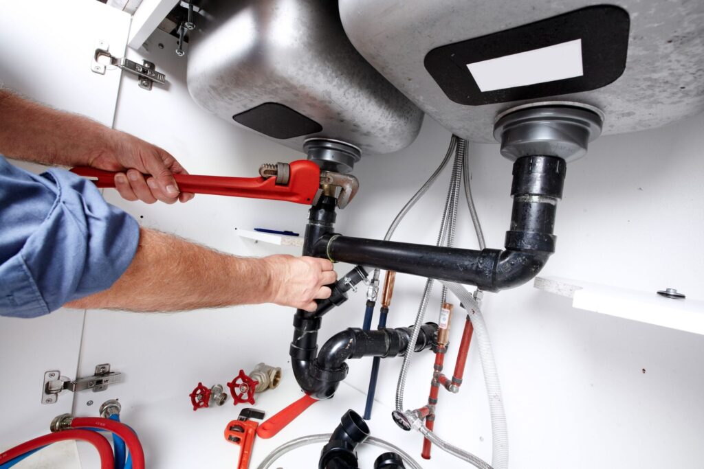 Plumber repairing drain pipes beneath a kitchen sink in Salinas